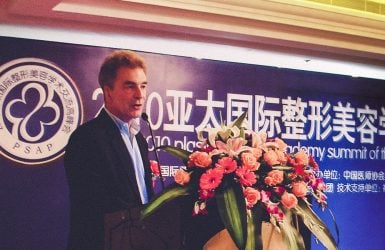 A suited man speaks at a conference podium with a "PSAP" banner and floral decoration.
