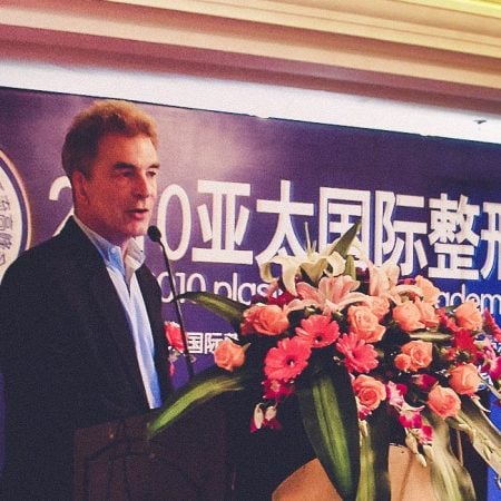 A suited man speaks at a conference podium with a "PSAP" banner and floral decoration.