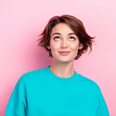 A person with short brown hair in a turquoise shirt looks thoughtfully upward against a pink background.