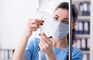 A healthcare worker in blue adjusts an IV drip in a medical facility.