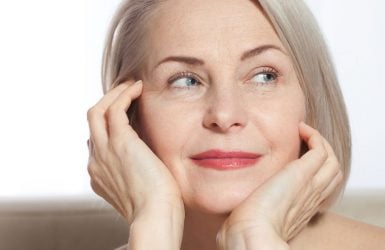 Gray-haired woman with a thoughtful expression rests her chin on hands