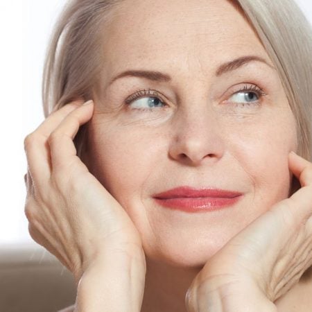 Gray-haired woman with a thoughtful expression rests her chin on hands