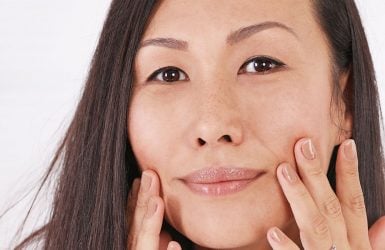 A person with long dark hair touches their cheeks