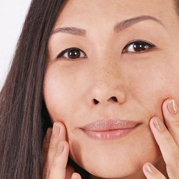 A person with long dark hair touches their cheeks