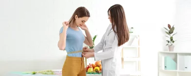 Doctor measures woman's waist; health focus with fruits and vegetables in background.