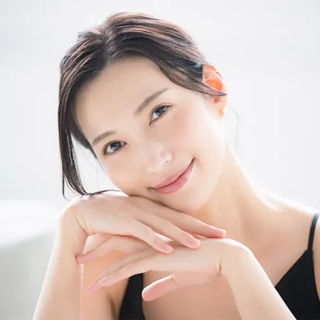 Dark-haired person in black top rests chin on hands; serene
