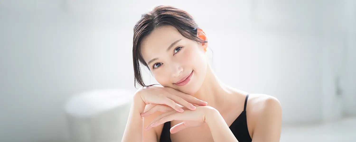 plastic-surgery-hawaii-hero-1 Dark-haired person in black top rests chin on hands; serene