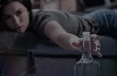 A person on a couch reaches for an empty bottle