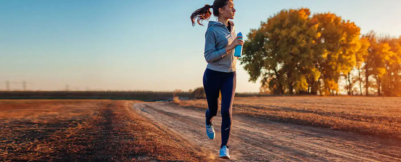 Woman jogging on dirt path at sunset