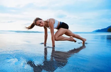 A woman exercises on a beach in a mountain climber pose