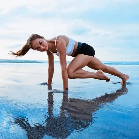 A woman exercises on a beach in a mountain climber pose