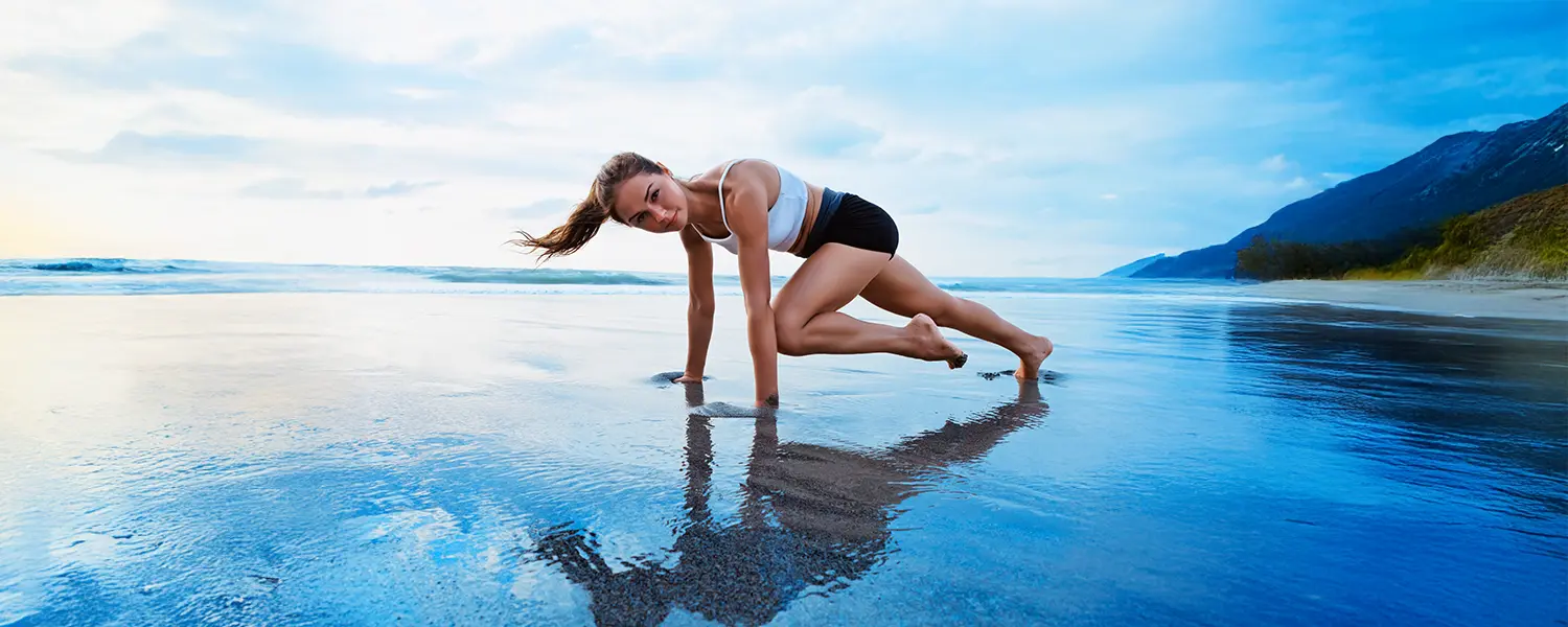 A woman exercises on a beach in a mountain climber pose