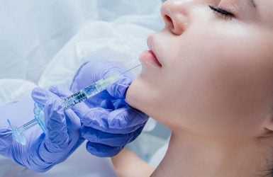 A person receives a chin injection from a gloved professional while lying down with eyes closed.