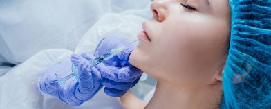 A person receives a chin injection from a gloved professional while lying down with eyes closed.