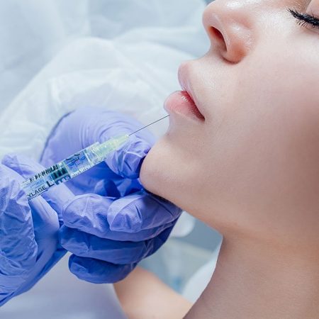 A person receives a chin injection from a gloved professional while lying down with eyes closed.