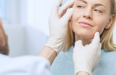 A gloved professional examines a woman's face in a clinical setting