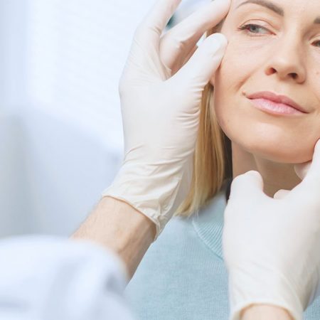 A gloved professional examines a woman's face in a clinical setting