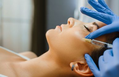 A professional injects a substance into a person's cheek in a clinical setting.