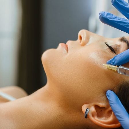 A professional injects a substance into a person's cheek in a clinical setting.