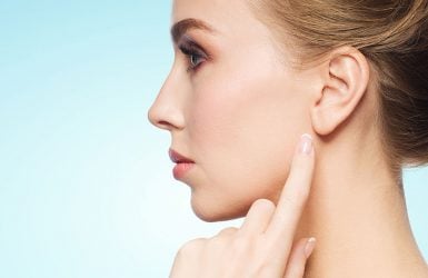 Woman with styled hair touching ear against light blue background.