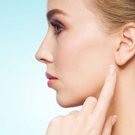 Woman with styled hair touching ear against light blue background.