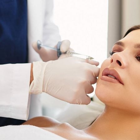 A professional gives a facial injection to a relaxed woman in a treatment room.