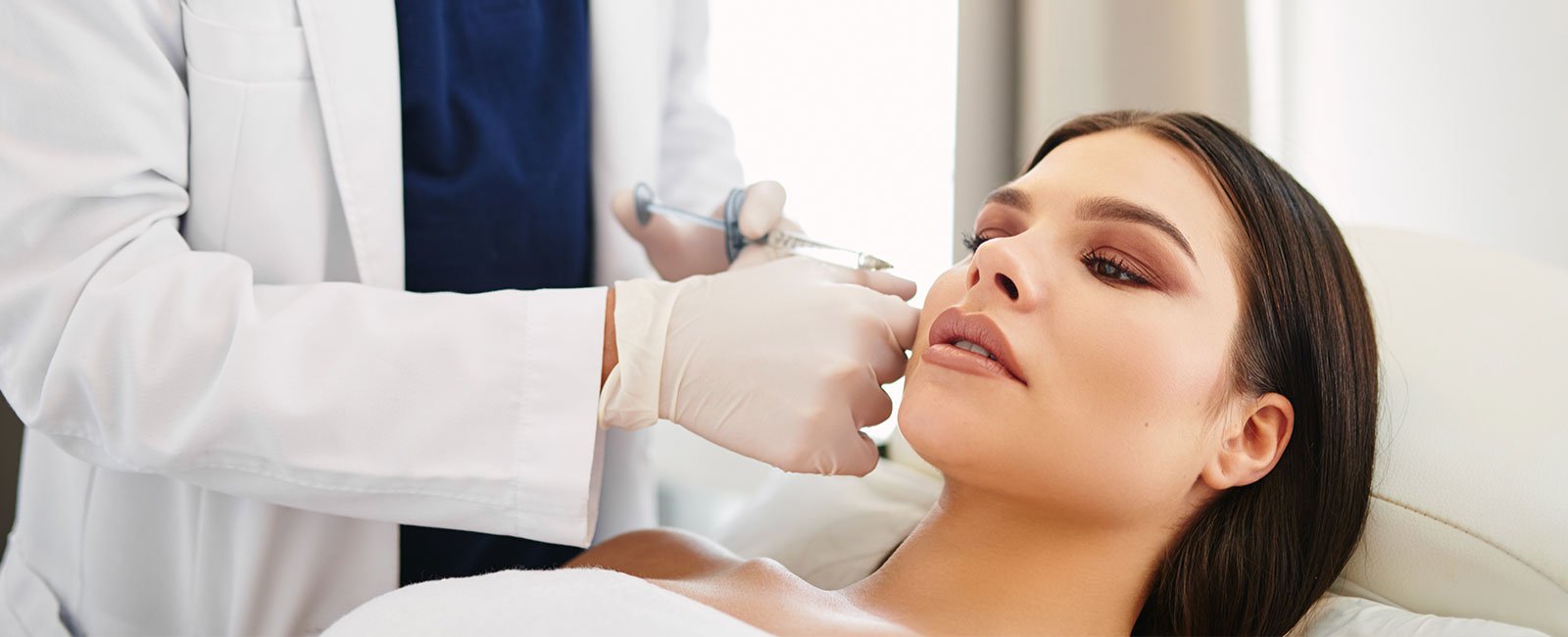 A professional gives a facial injection to a relaxed woman in a treatment room.