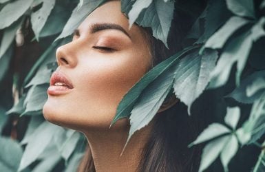 A serene woman with closed eyes is surrounded by lush leaves