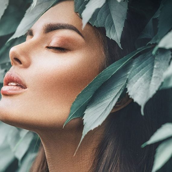 A serene woman with closed eyes is surrounded by lush leaves