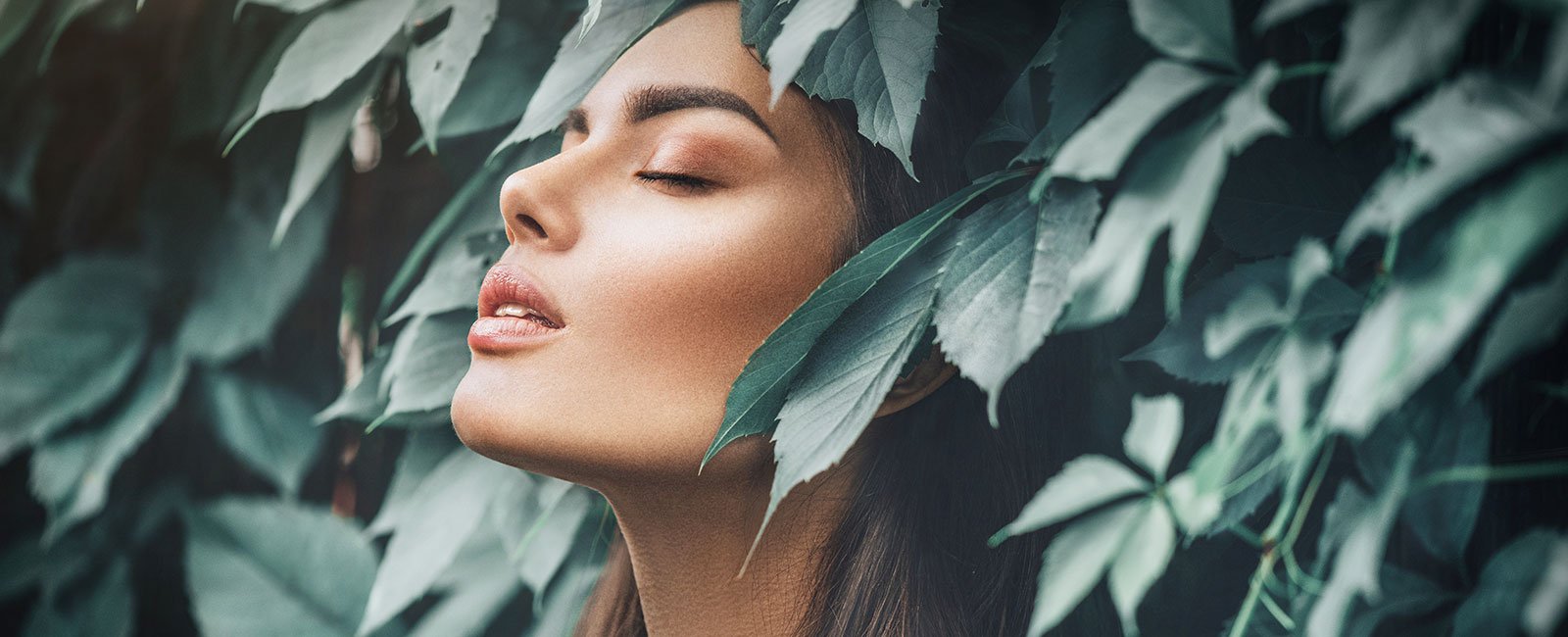 A serene woman with closed eyes is surrounded by lush leaves