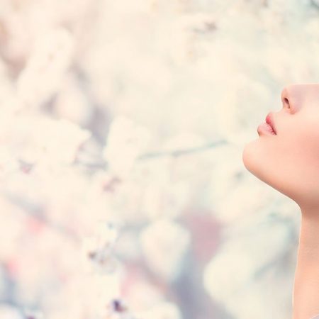 A serene woman with long brown hair is shown in profile against a blurred background of white flowers.