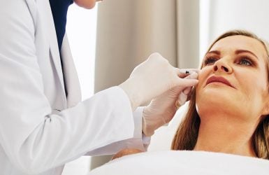 A healthcare professional injects a patient's cheek in a well-lit room.
