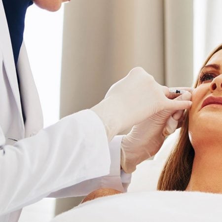 A healthcare professional injects a patient's cheek in a well-lit room.