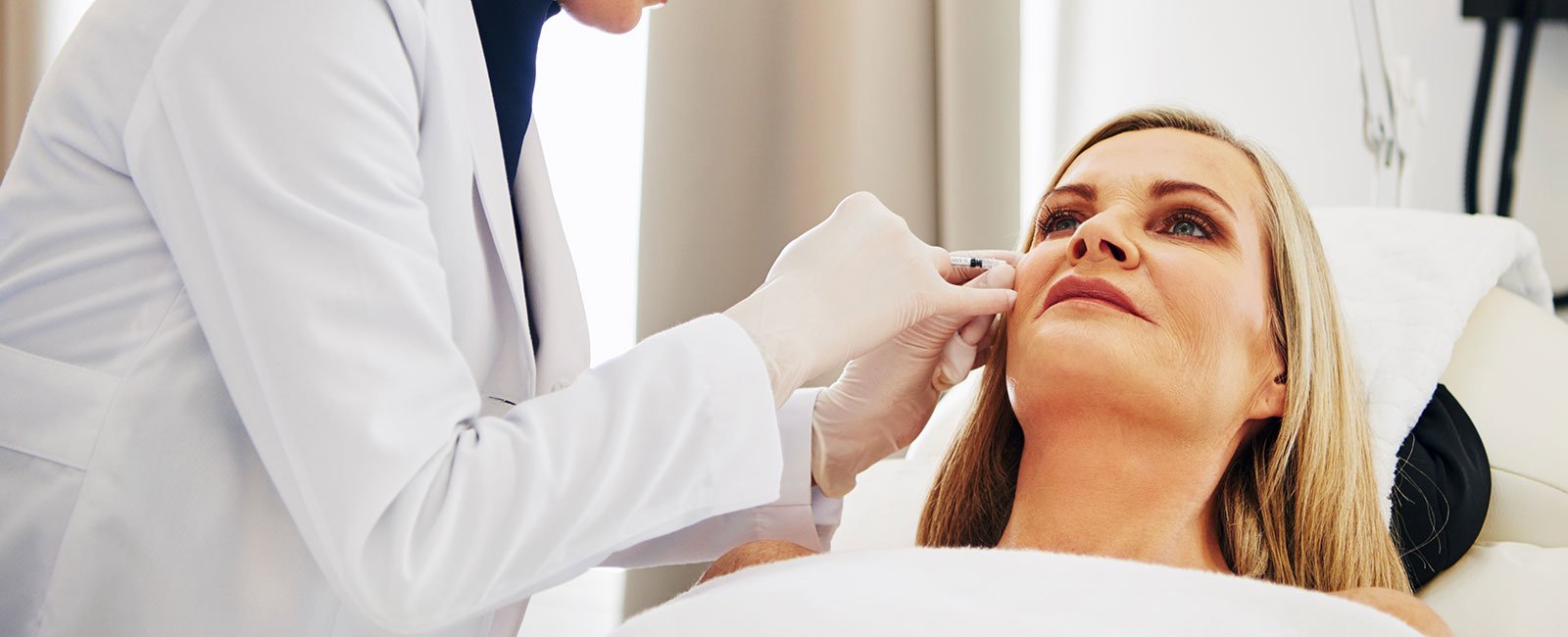 A healthcare professional injects a patient's cheek in a well-lit room.
