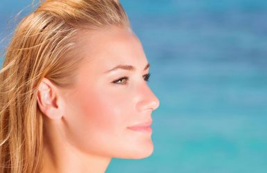 A blonde person gazes calmly at the ocean under a clear blue sky