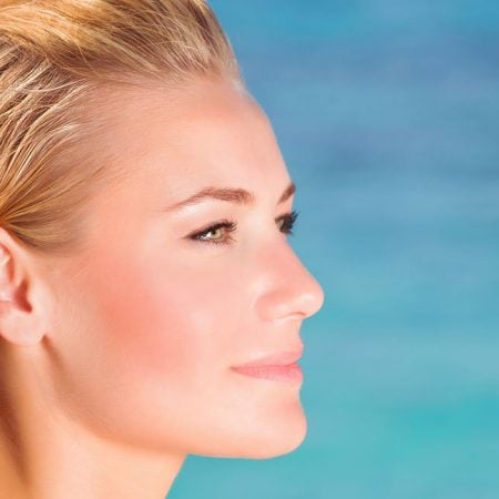 A blonde person gazes calmly at the ocean under a clear blue sky