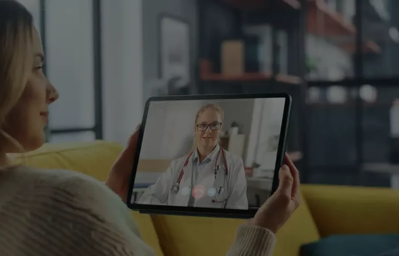 Woman on yellow couch video calls doctor on tablet; modern living room background.