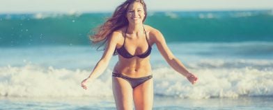 Woman in black bikini smiles by ocean
