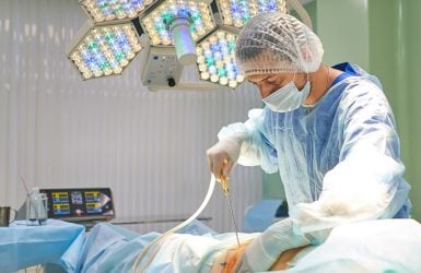 A plastic surgeon operates under surgical lights